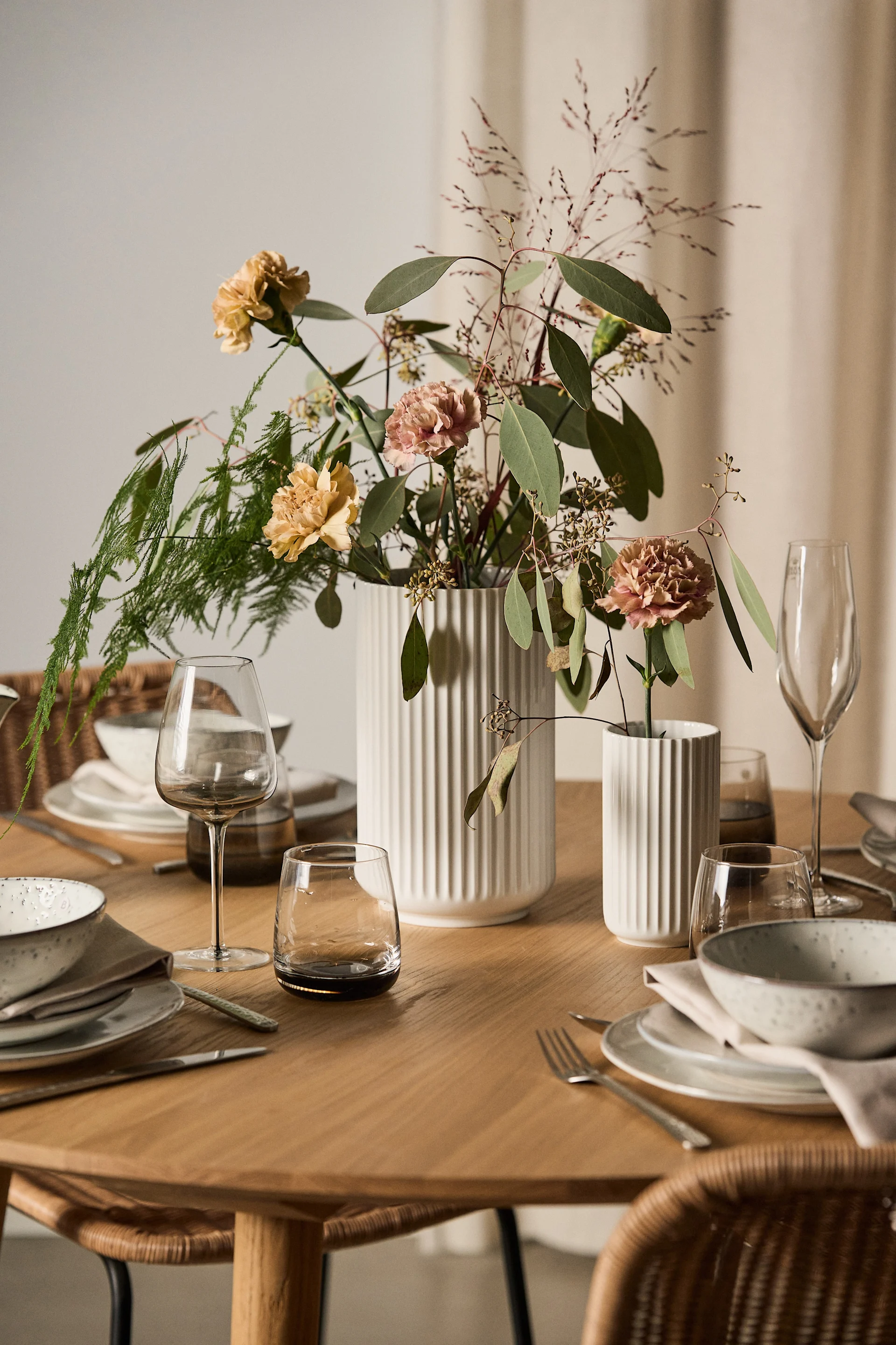 Kukat ja sopiva maljakko ovat mukava lahja ystävänpäiväksi. Tässä on kaksi valkoista Lyngby-maljakkoa, joissa on kukkia katetulla pöydällä.