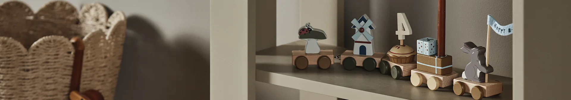 Puinen lelujuna hyllyllä, vaunuissa leppäkerttu, tuulimylly, cupcake "4"-kynttilällä, lahja ja pupu, jolla on "Happy B" -lippu.