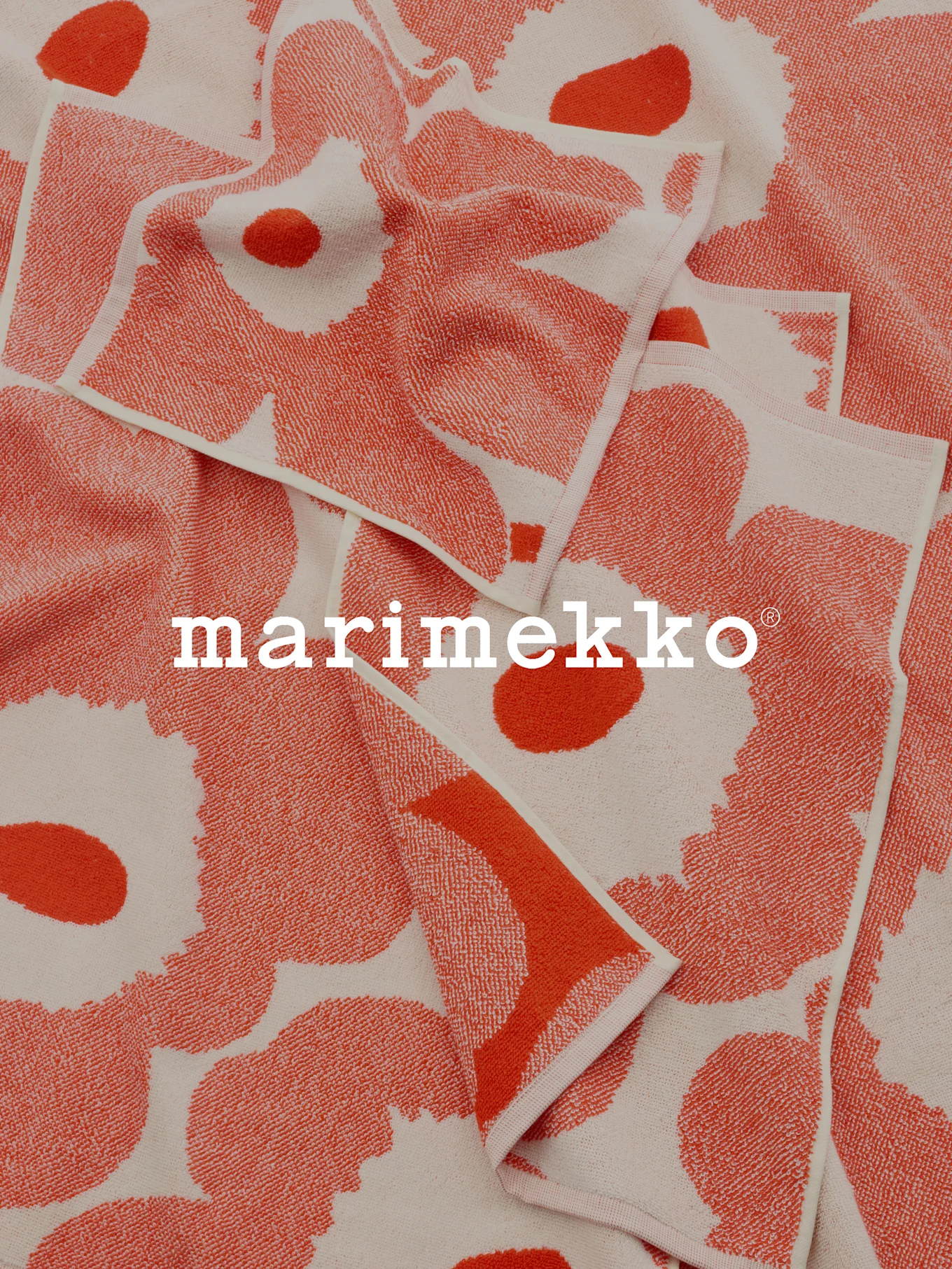 Taitettuja korallinpunaisia ja luonnonvalkoisia kuvioituja pyyhkeitä Marimekko-logolla.
