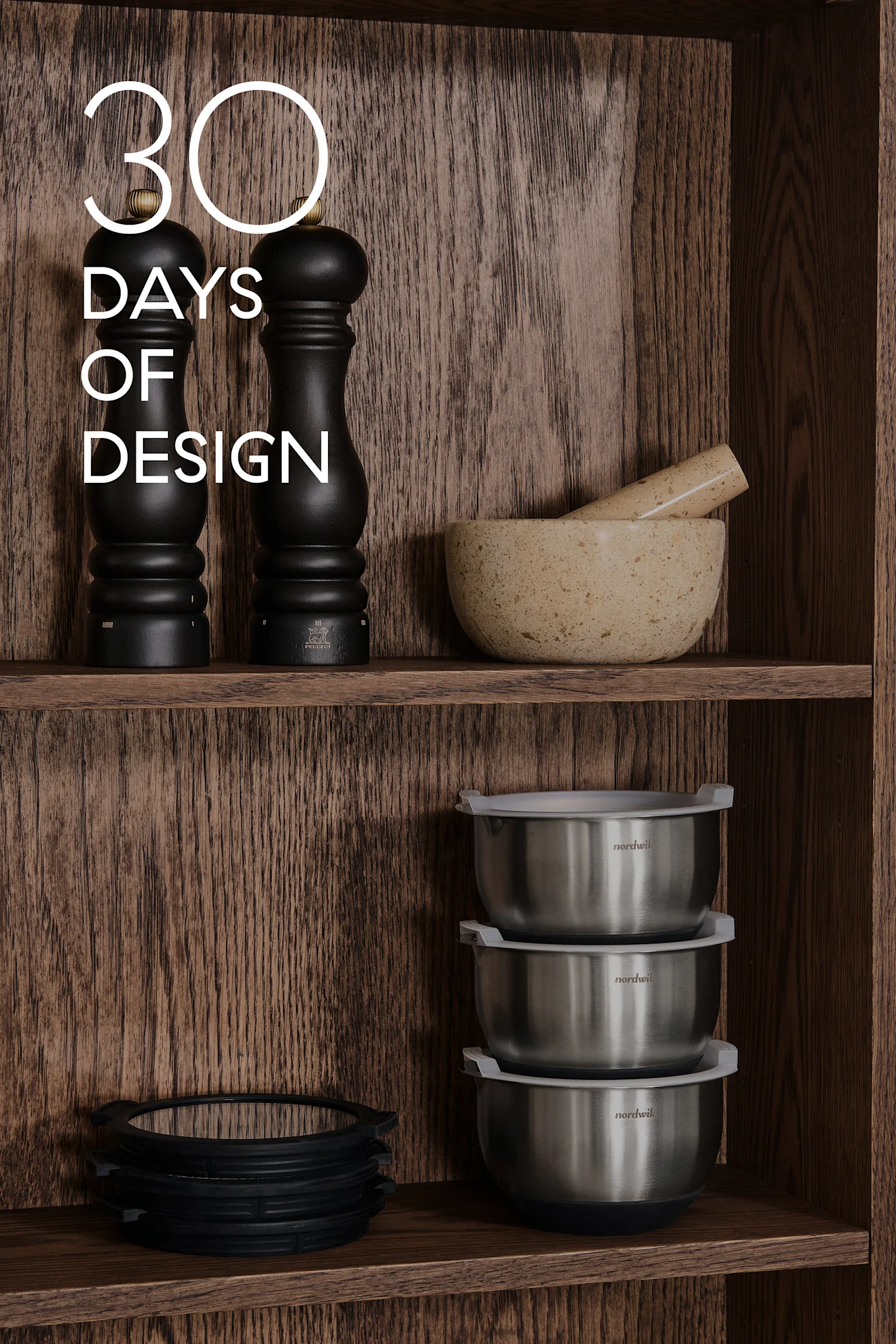 Puuhyllyillä keittiövälineitä: mustat myllyt, mortteli & survin, teräskulhot, silikonirenkaat. Teksti: 30 DAYS OF DESIGN.