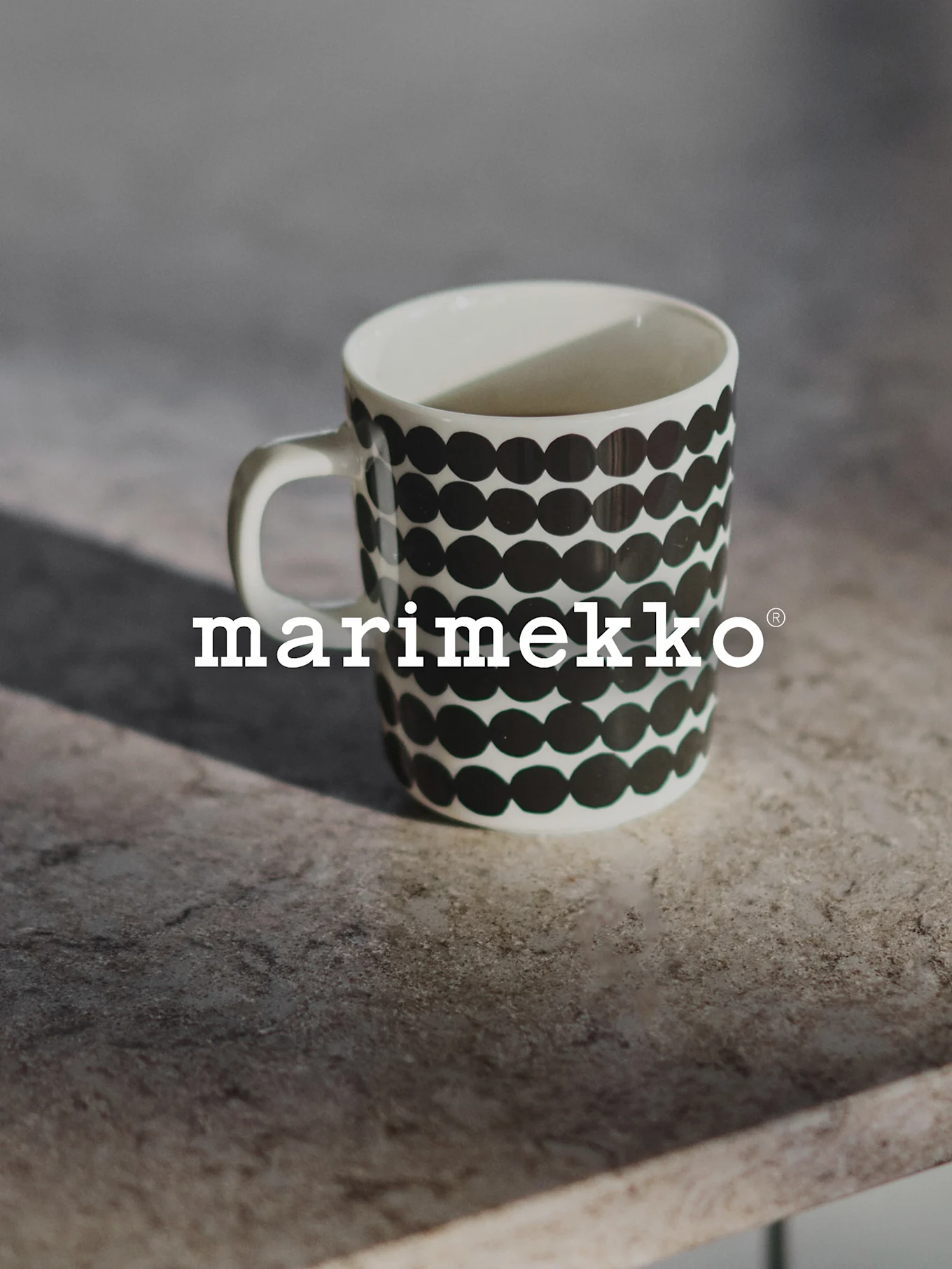 Valkoinen Marimekko-muki mustalla pilkkukuvioinnilla harmaalla pinnalla.