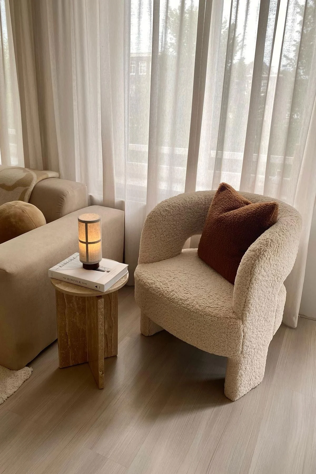 Marmorisen sohvapöydän päällä on kirja, jonka päällä on Audo Copenhagenin Hashira-pöytävalaisin, vasemmalla puolella sohva ja oikealla puolella nojatuoli.