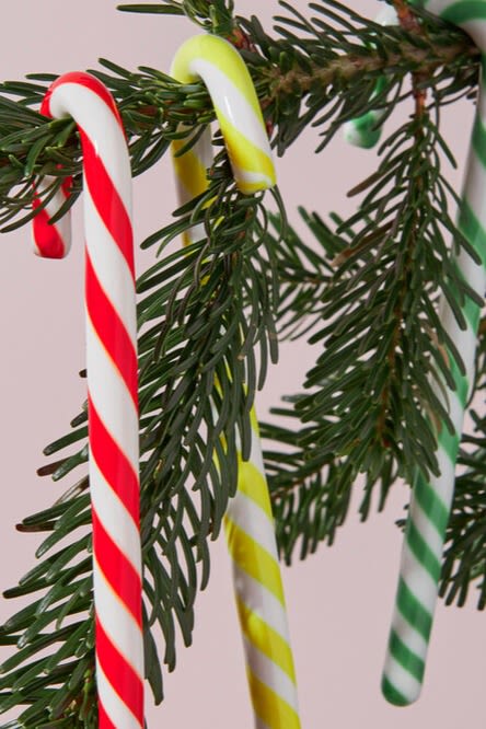 Käsi asettaa joulukuuseen suuren käärityn karkkikoristeen, joka on leikkisä ja värikäs joulukuusen koristeluidea.
