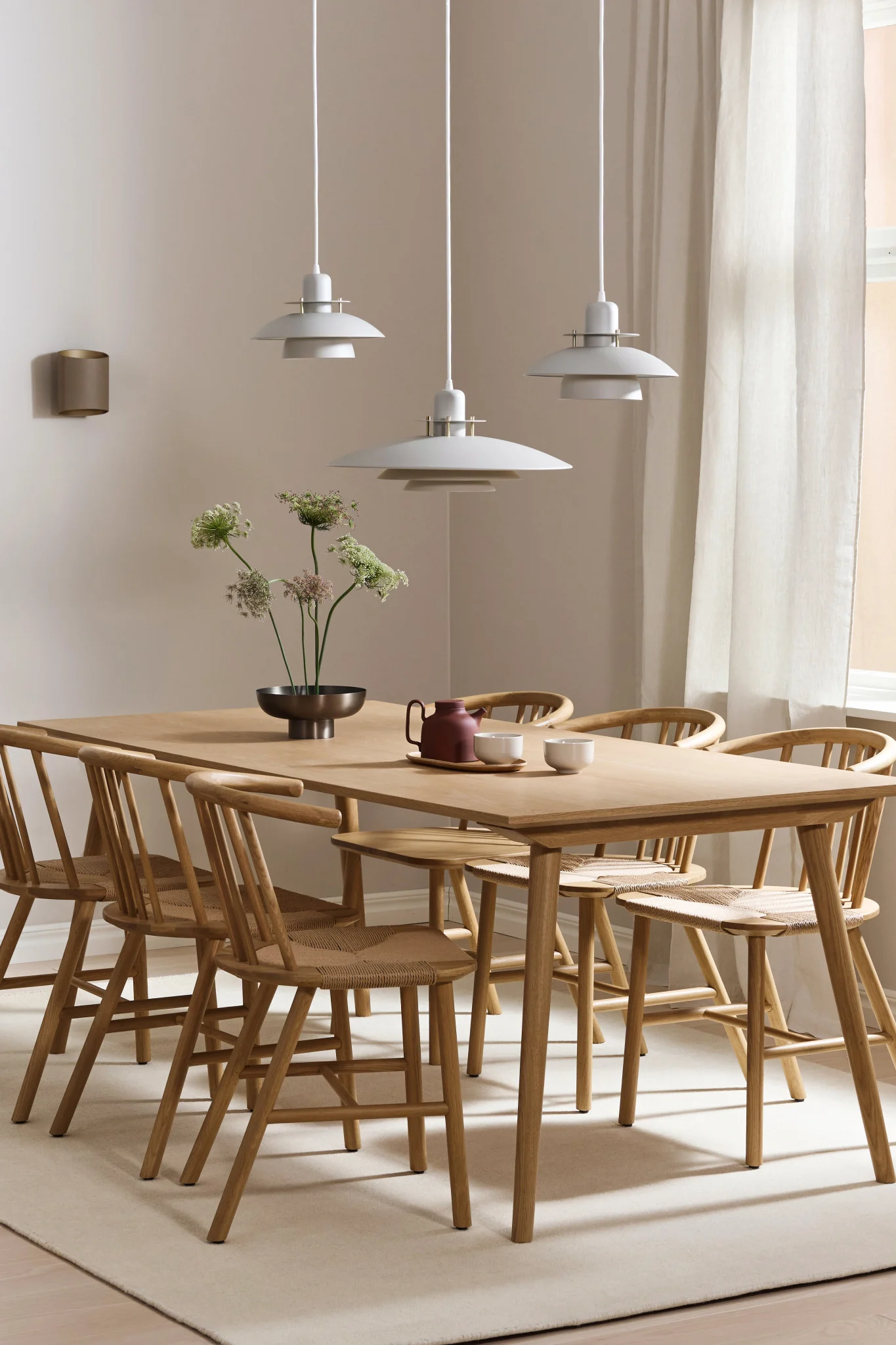 Tässä näet ruokasalin valaistusideoita pitkälle pöydälle. Picasso-valaisin roikkuu kolmen valaisimen rivissä ja Sinne-valaisin seinällä. 