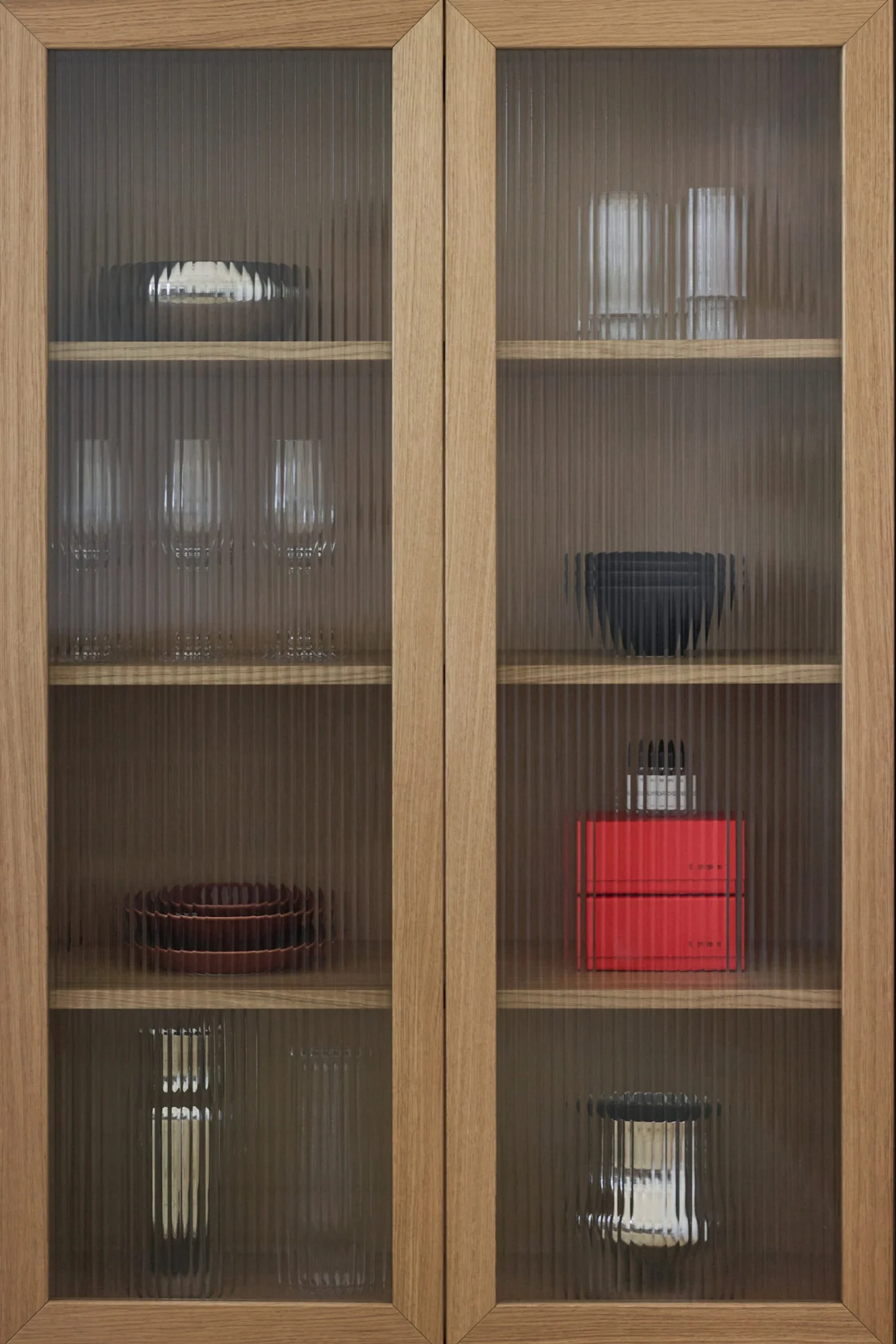 Puinen kaappi, jossa uurrettuja lasiovia, esillä erilaisia astioita, laseja ja koriste-esineitä hyllyillä.