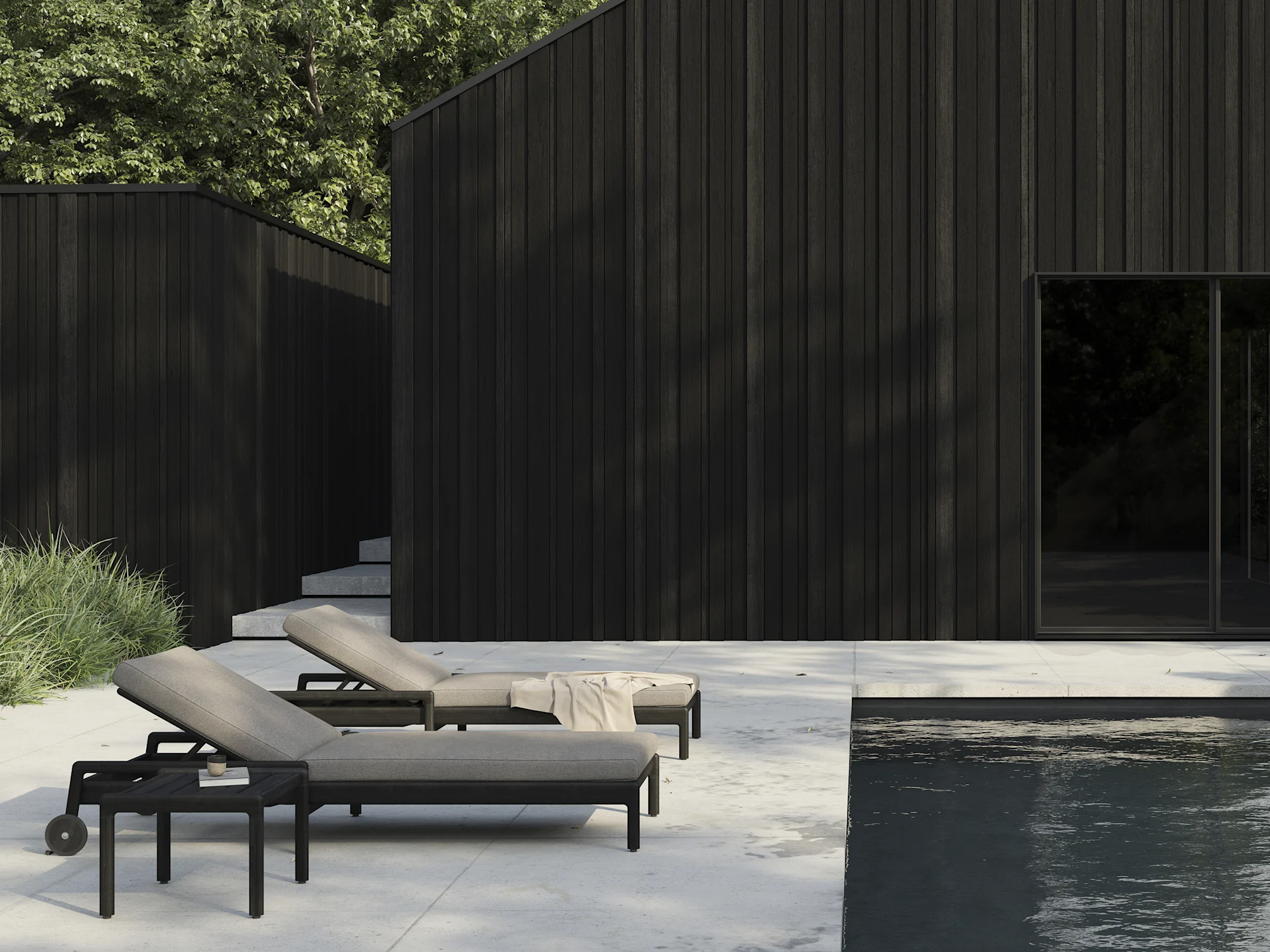 Kaksi tummaa aurinkotuolia vaaleilla pehmusteilla patiolla uima-altaan vieressä, taustalla modernit tummat puurakennukset.