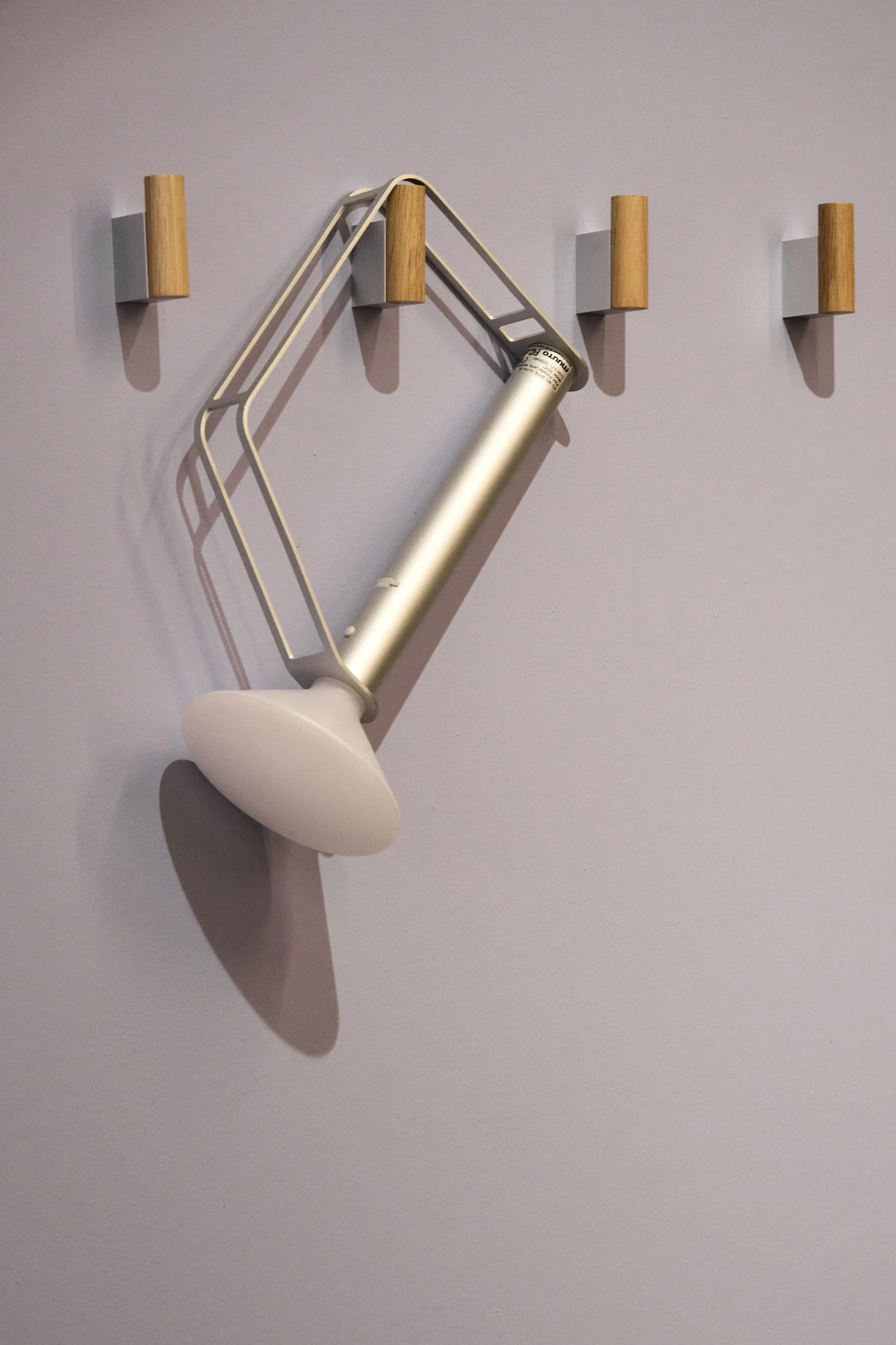 Muuton hopeinen, kannettava Piton-pöytävalaisin roikkuu yhdessä neljästä koukusta seinällä.