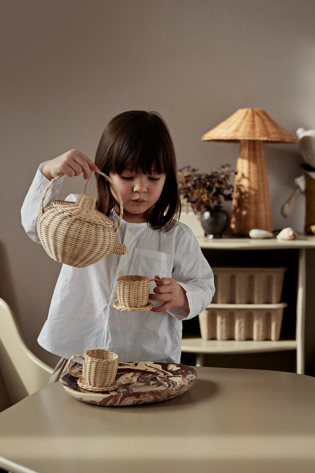 Lapsi leikkii kaatavansa teetä koripussista. Leikkisät ja tyylikkäät lelut ovat täydellisiä esille laitettavia esineitä lastenhuoneeseen. 