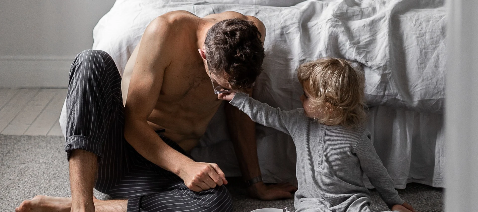 Tässä näet miehen, jolla on pieni lapsi ja joka istuu sängyn edessä.