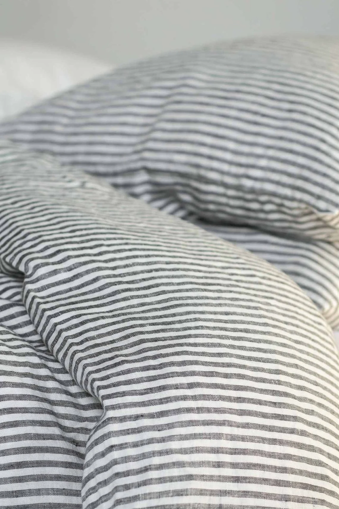 Lähikuva myllätyistä vuodevaatteista, joissa on mustavalkoraidallinen pellavapussilakana.