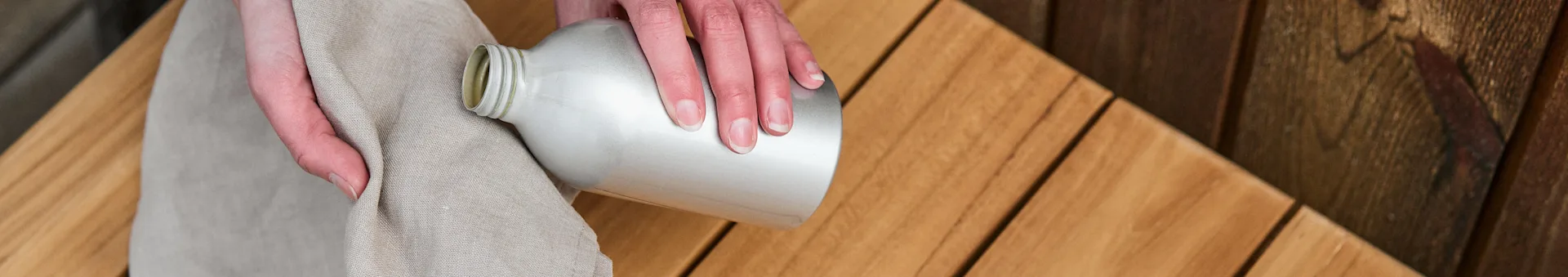 Käsipari pitelee liinaa ja tiikkiöljypulloa valmiina öljyämään Nordic Nestin tiikkipenkkiä merkiltä 1898. 