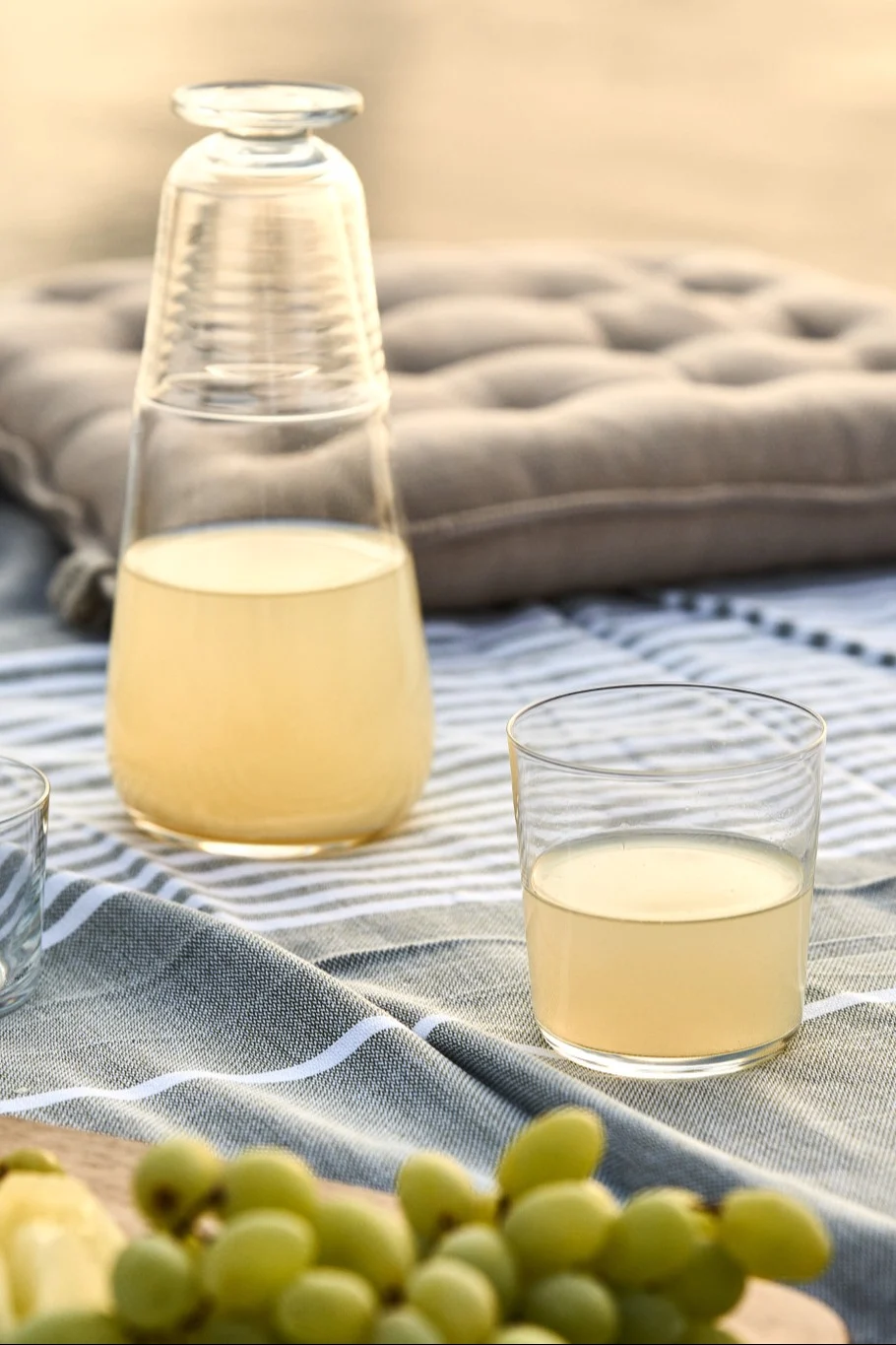 Löydä yksinkertaisia kesäreseptejä: tässä näet pullon sitruunamehua lasin ja rypäleterttujen kanssa piknikpöydällä.