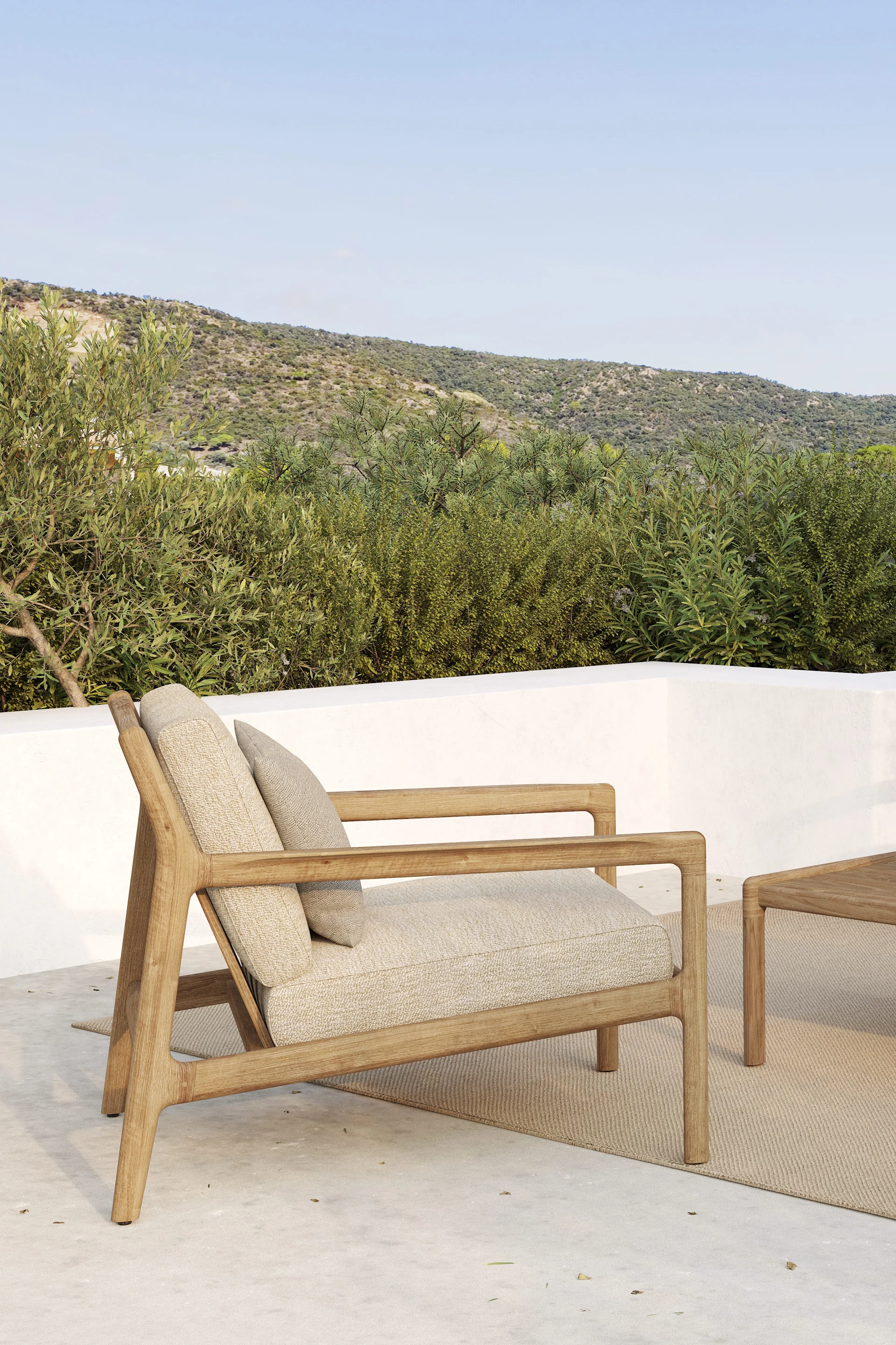 Ulkokäyttöön tarkoitettu puinen nojatuoli vaaleilla tyynyillä terassilla, taustalla vihreät kukkulat ja sininen taivas.