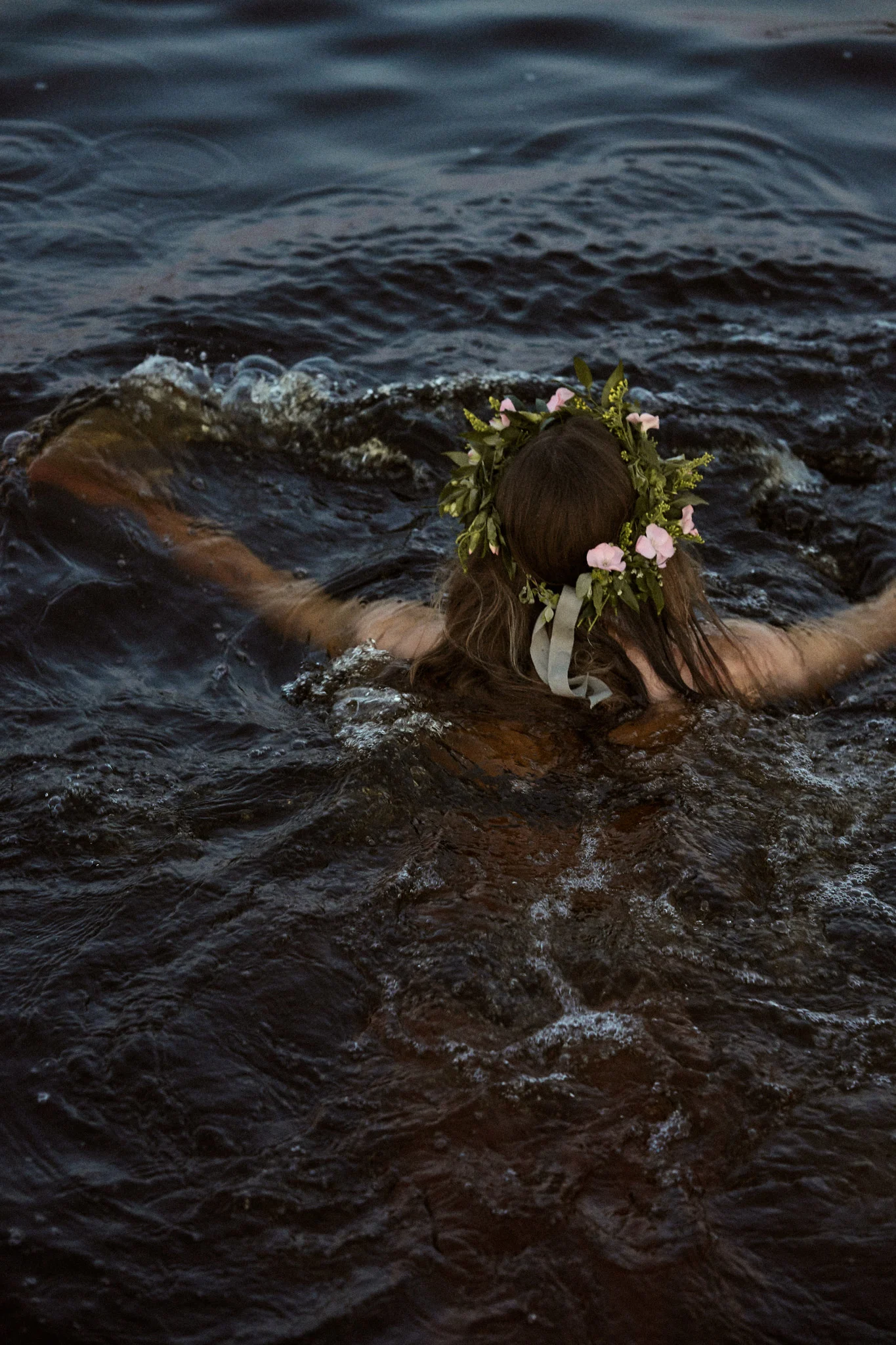 Nainen ui järvessä juhannusseppele päässään.