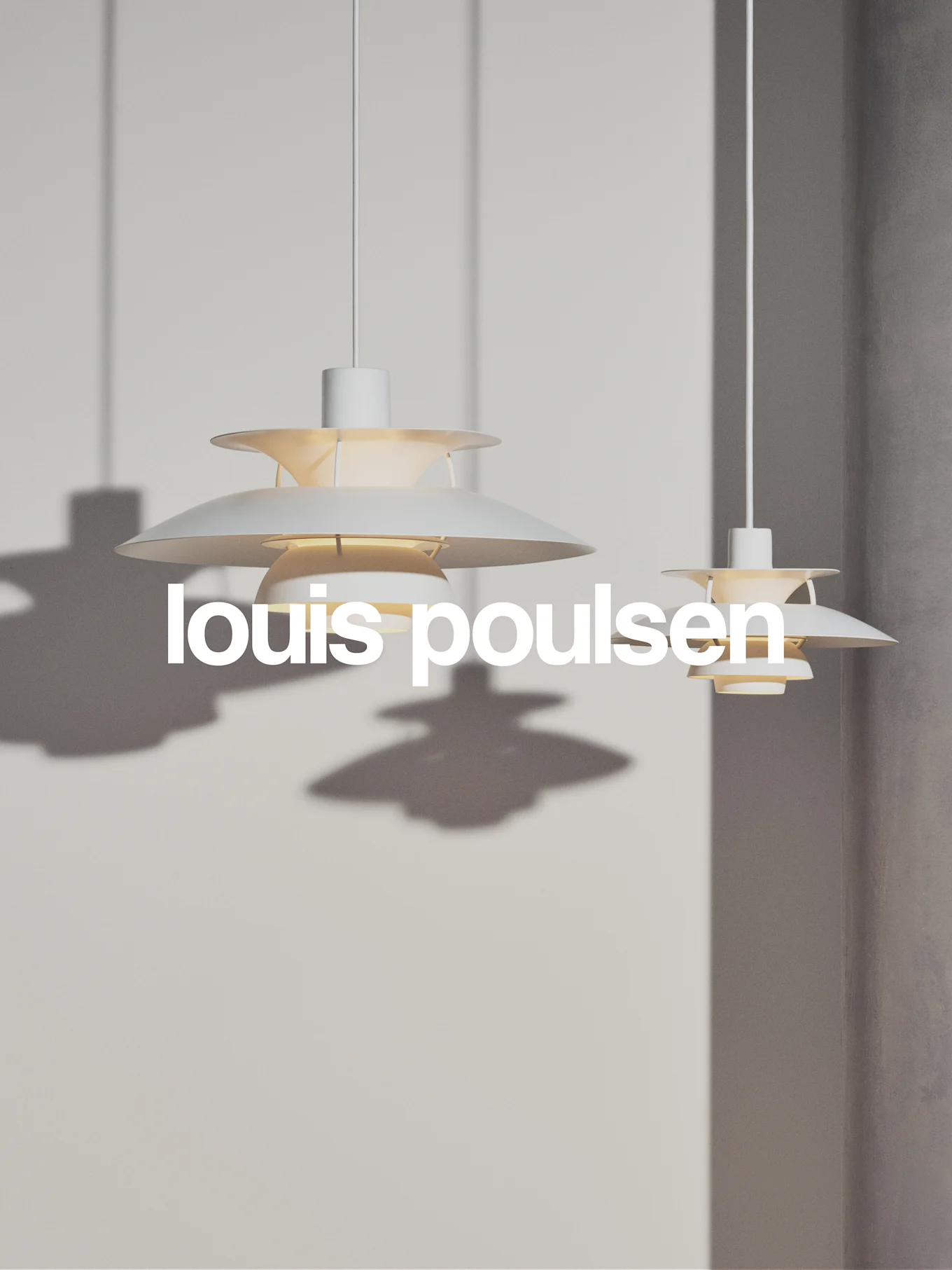 Kaksi valkoista, kerroksellista riippuvalaisinta roikkuu vaaleanharmaalla seinällä, tekstillä 'louis poulsen'.