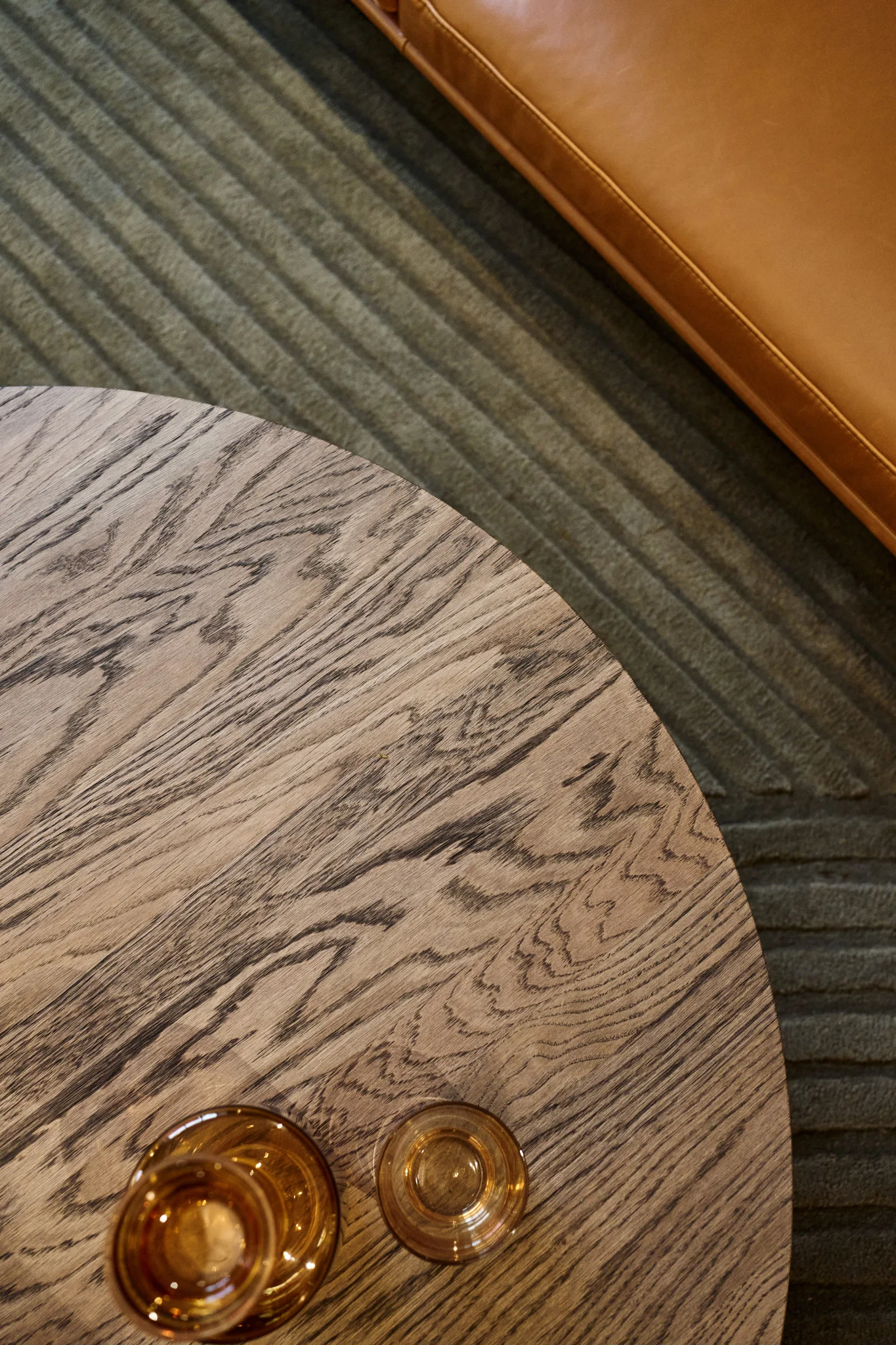 Sohvapöytä, jossa on tummanruskea pöytälevy, seisoo sohvan edessä, ja sen päällä on useita Muuton Raise-malliston meripihkanvärisiä laseja.