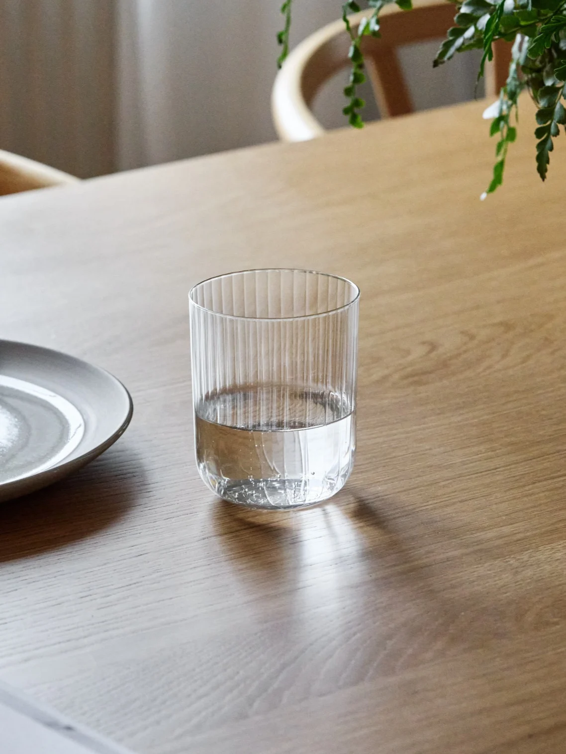 Uurteinen lasilasi, puoliksi vedellä täytettynä, seisoo puupöydällä keraamisen lautasen vieressä.