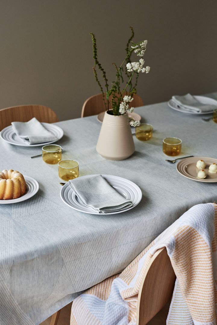 Tyylikäs pöytäasetelma NJRD:n pehmeillä pastelliväreillä, jossa on sininen pöytäliina ja sinikeltainen heitto.