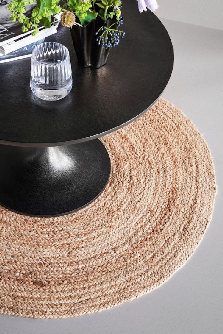 House Doctorin pyöreä juuttimatto Rugy, joka sopii materiaalinsa ansiosta erinomaisesti boho-tyyliseen sisustukseen, on sijoitettu pyöreän mustan pöydän alle.