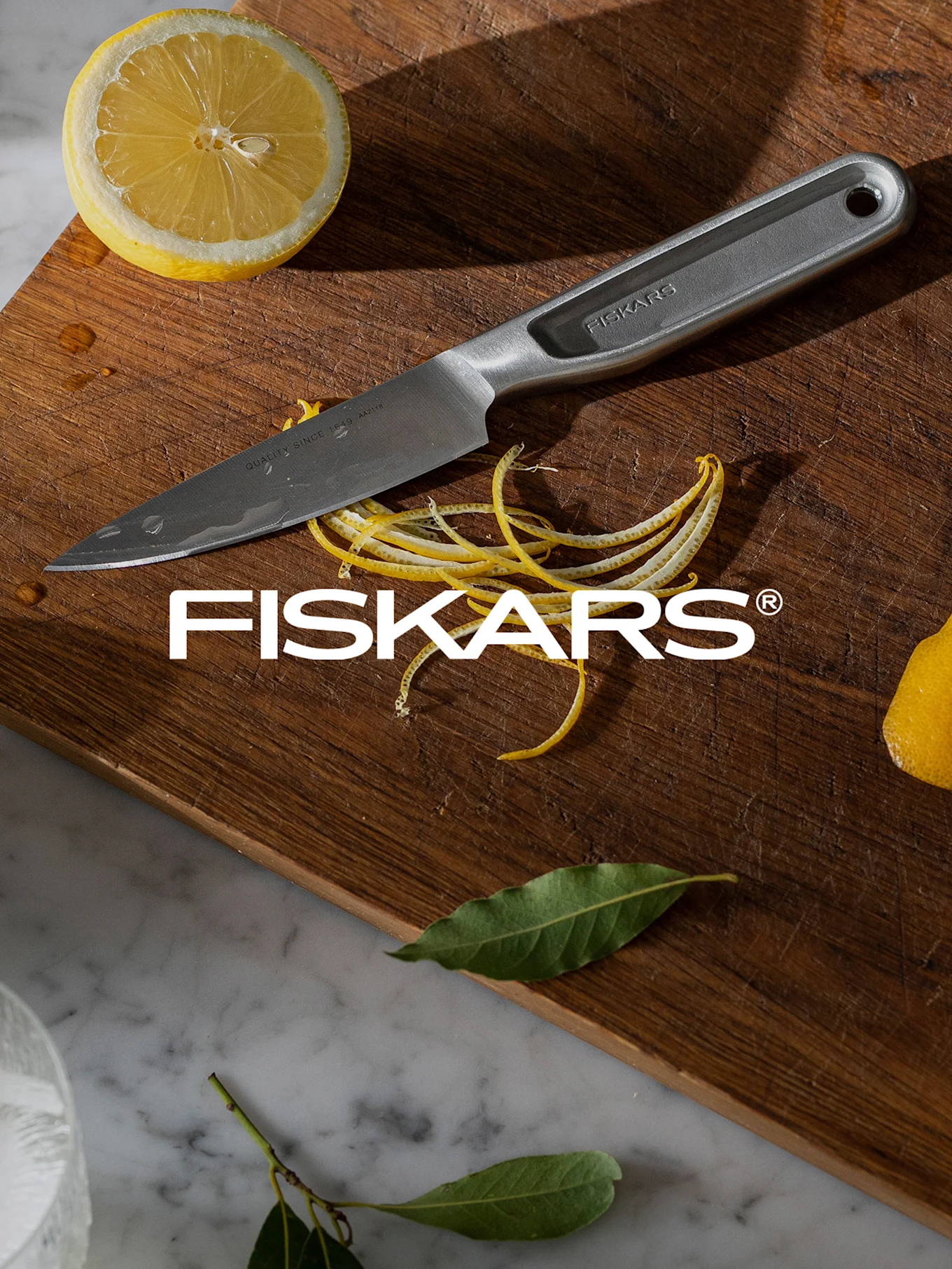 Fiskars-veitsi puisella leikkuulaudalla puolikkaan sitruunan, sitruunankuoren ja vesipisaroiden kanssa.