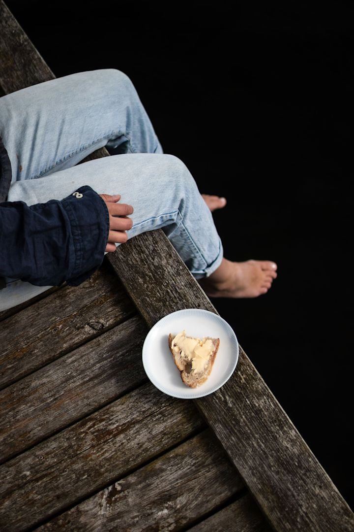 Lagom: Nainen istuu laiturilla, vieressään Wik&Walsoen Osean-lautanen, jolla on voileipä.