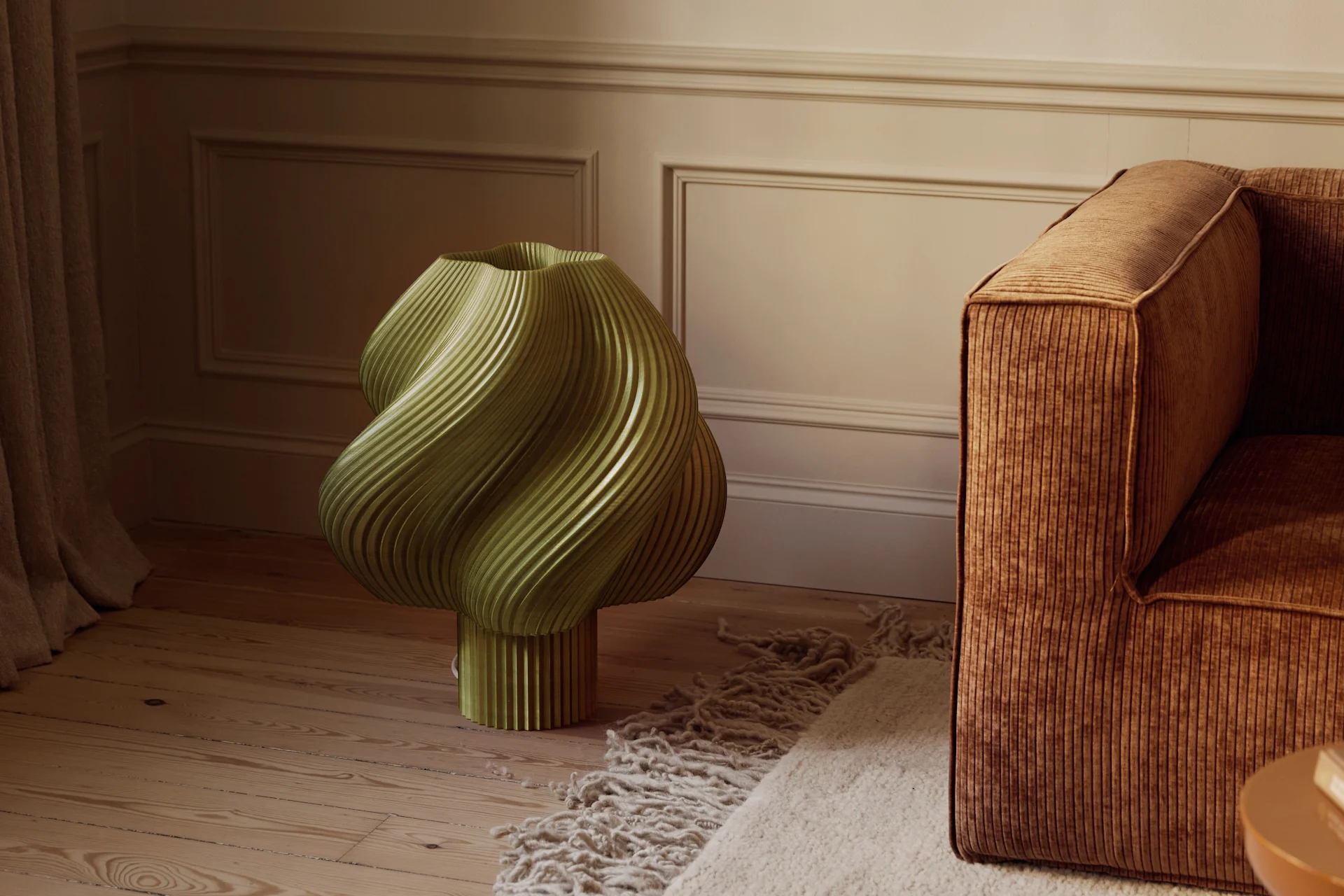 Oliivinvihreä, veistoksellinen, uurrettu esine puulattialla ruskean vakosamettisohvan ja tekstuurimaton vieressä huoneessa, jossa on muotoillut seinät.