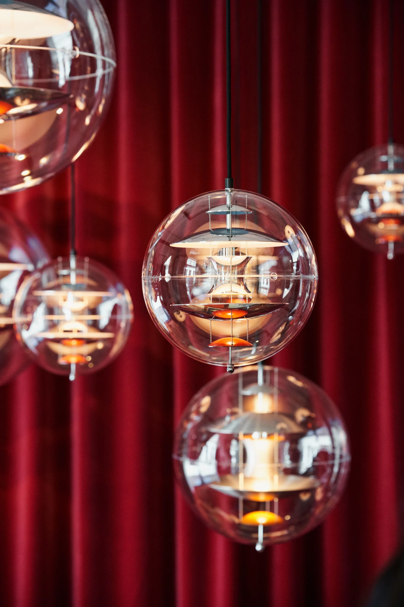 Useita Verpanin Globe Glass -riippuvalaisimia roikkuu katosta punaisen verhon edessä.