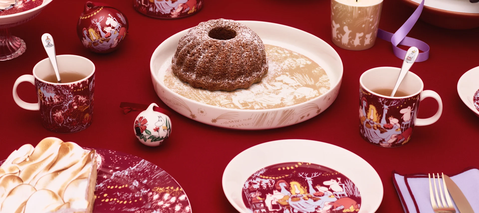 Moomin Arabian erilaisia Muumi-kuppeja seisoo pöydällä ulkona, leimasinkannun vieressä.