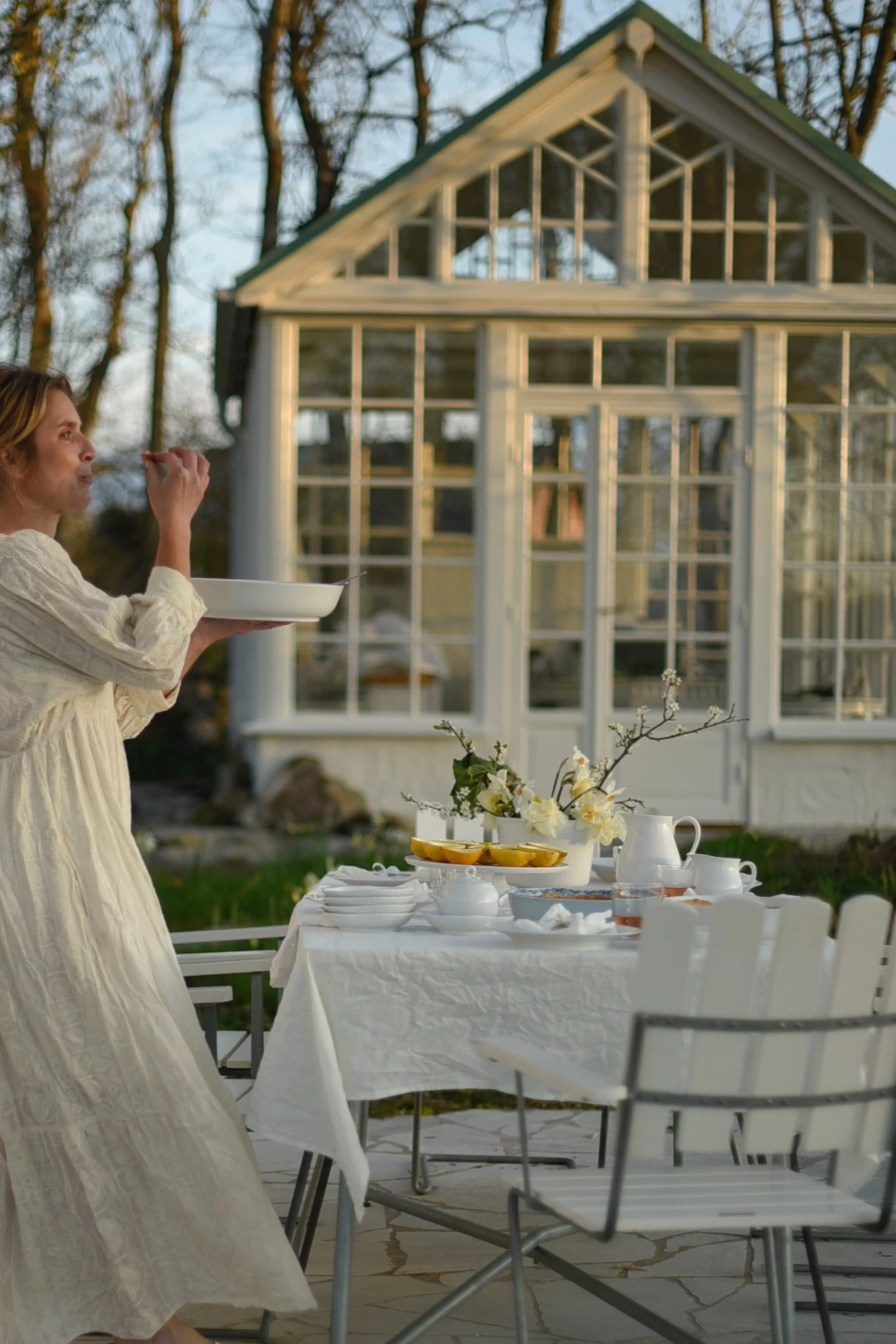 Grythyttanin valkoisilla A2-tuoleilla katettu pöytä seisoo kasvihuoneen edessä @khouri.julia:n puutarhassa.