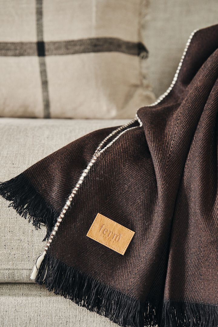 Herringbone viltti värissä dark brown merkiltä Ferm Living, fokuksessa kaunis etiketti.