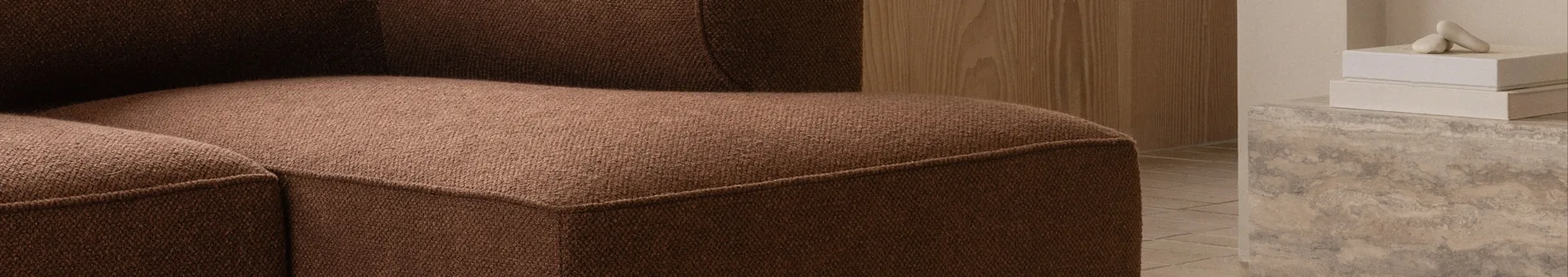 Lähikuva ruskeasta kuvioidusta sohvasta, puuseinän ja koriste-esineiden kera betonipinnalla taustalla.