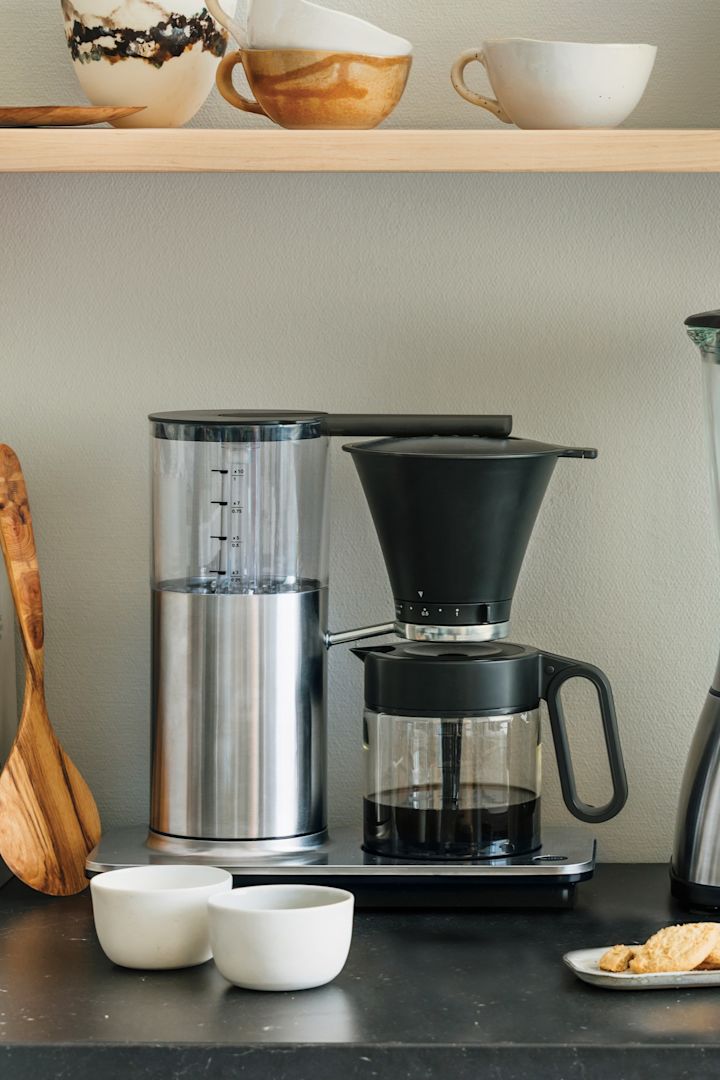 Tarvitset myös oikeat laitteet kodin kahvibaariin. Tässä näet Wilfan klassisen suodatinkahvinkeittimen seisomassa keittiön sivupöydällä, ja sen yläpuolella on hylly, jossa on kulhoja ja leivänpaahdin.