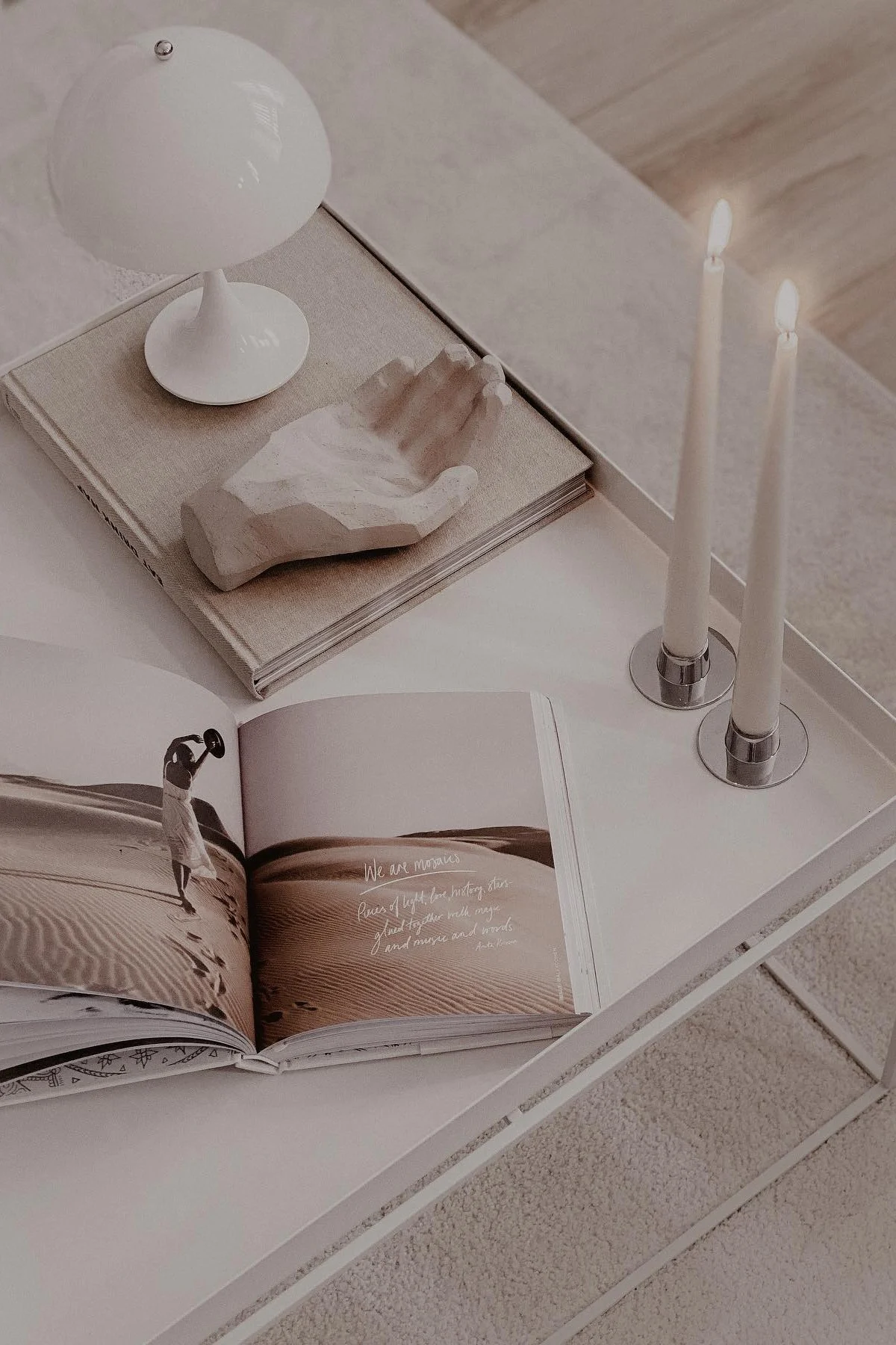 Leveä sohvapöytä, koristeltu kirjoilla, koristeellisella kädellä, kahdella kynttilällä ja Louis Poulsenin kannettavalla Panthella-pöytävalaisimella.