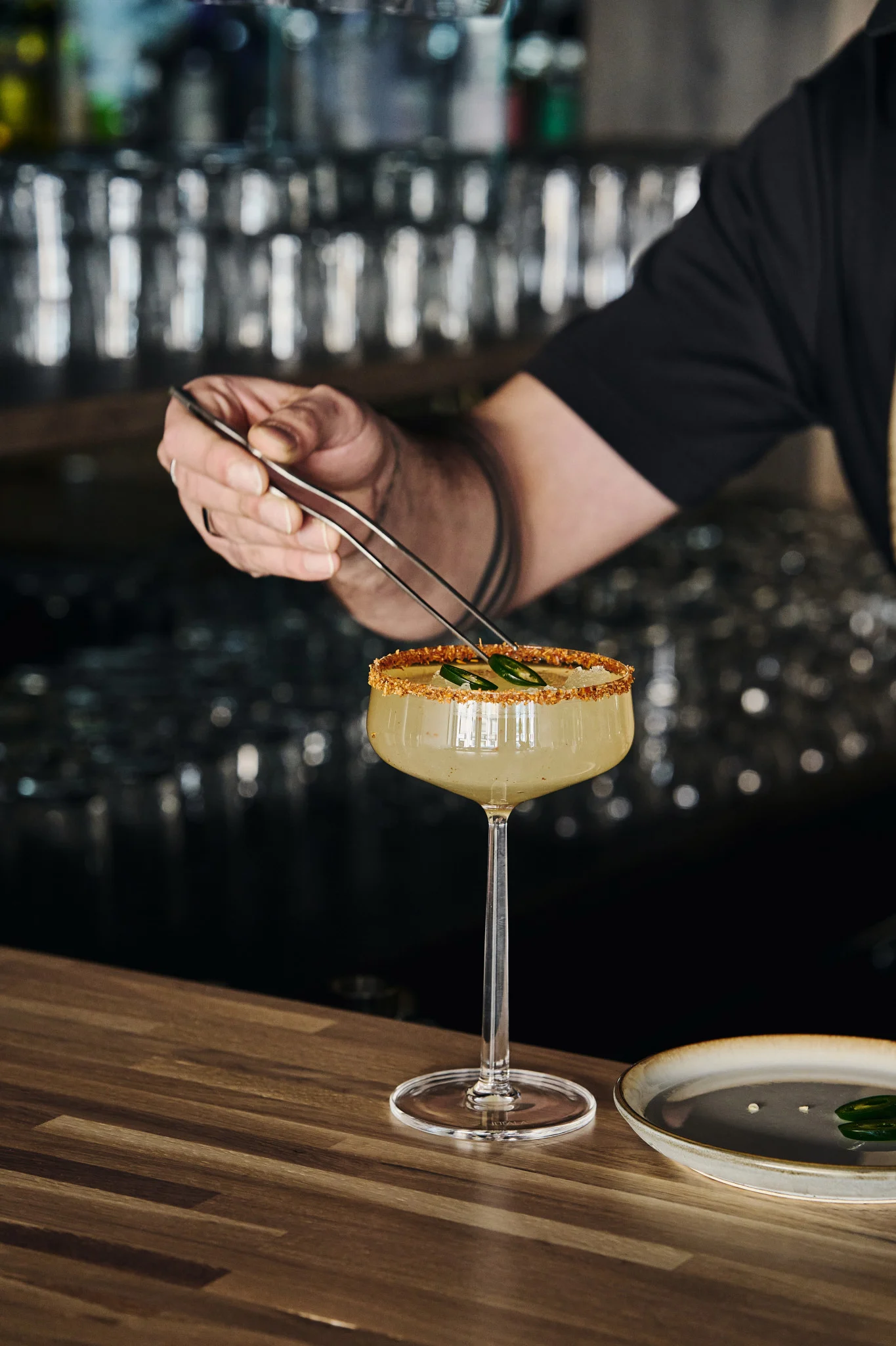 Täydellinen mocktaileille: Iittalan Essence-cocktail-lasi, jossa on juoma, koristeltu reuna ja jalapeño-viipaleita, jotka on asetettu pihdeillä.