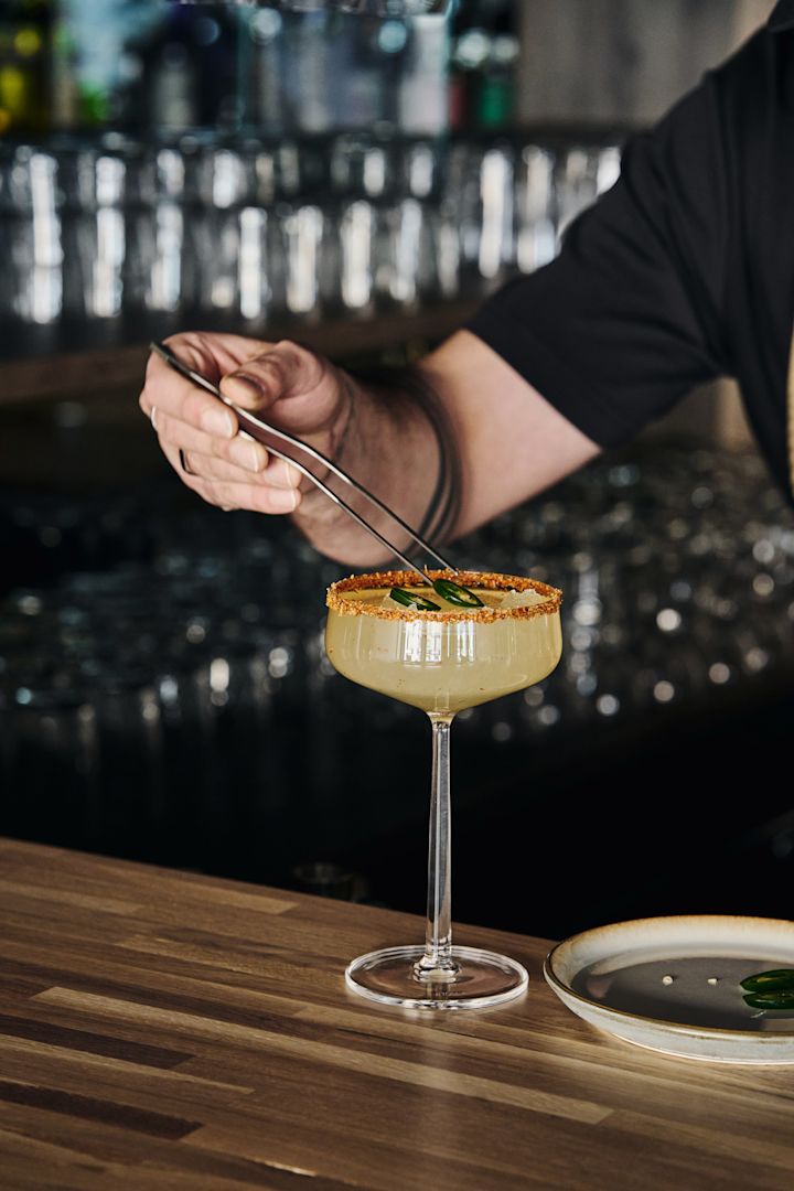 Täydellinen mocktaileille: Iittalan Essence-cocktail-lasi, jossa on juoma, koristeltu reuna ja jalapeño-viipaleita, jotka on asetettu pihdeillä.