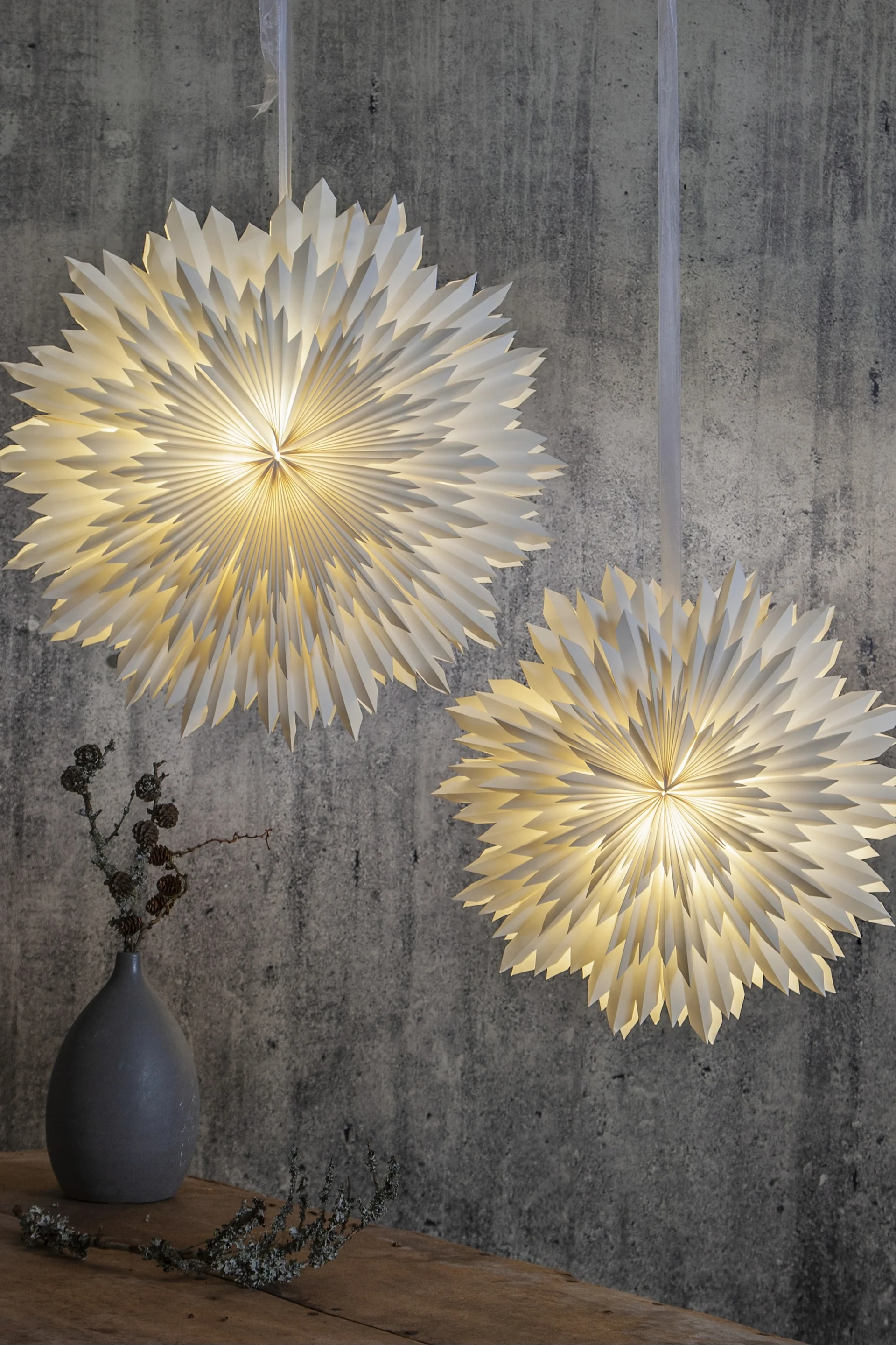 Star Tradingin joulutähti Ice roikkuu parina harmaata seinää vasten.