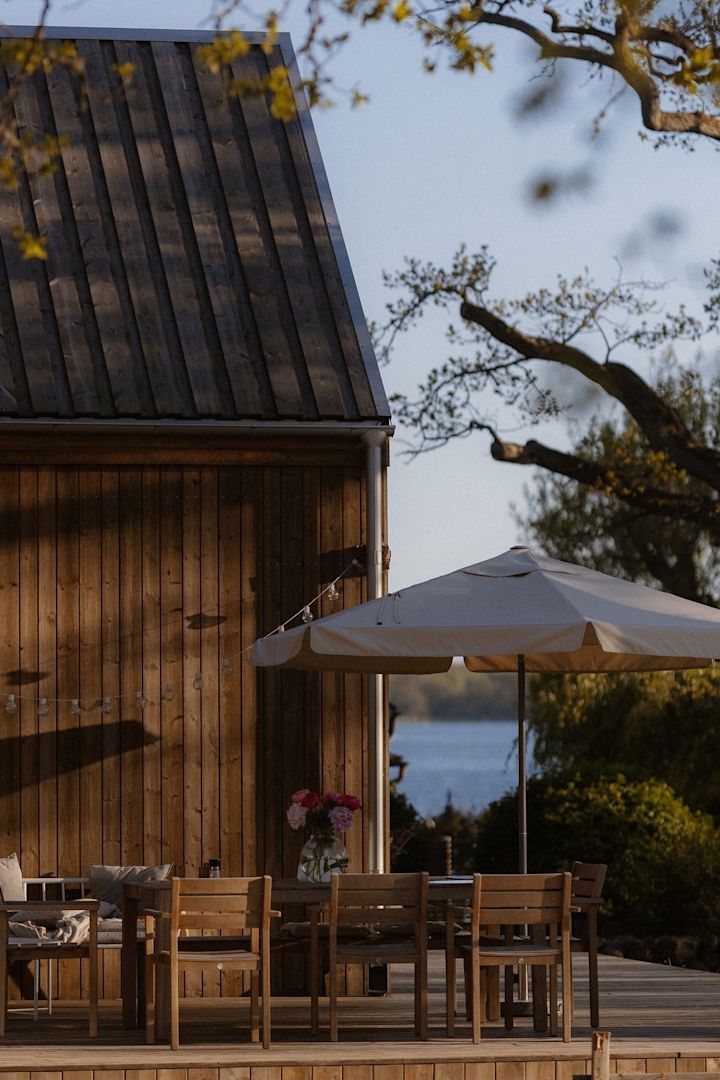 Viihtyisä patio puutalon edessä, jossa on ruokailutila, jossa on Sköndal-tuoleja vuodelta 1898 ja aurinkovarjo.