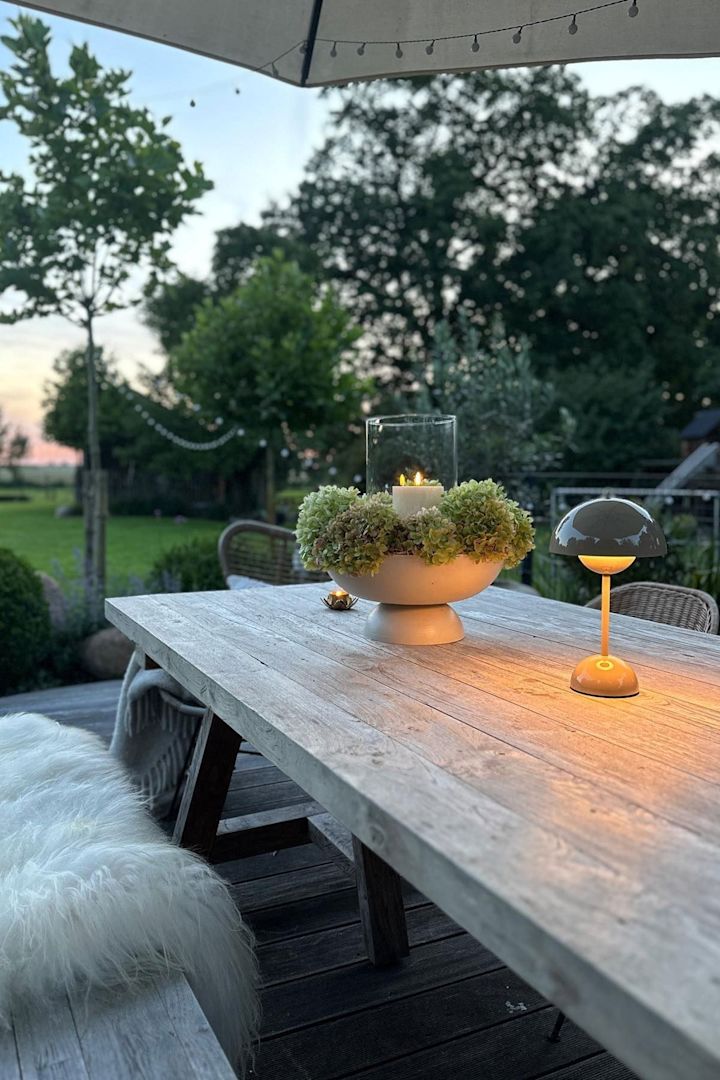 Viihtyisä terassi, jossa on suuri ruokapöytä ja penkkejä, koristeltu kynttilöillä ja &Traditionin Flowerpot-pöytävalaisimella.